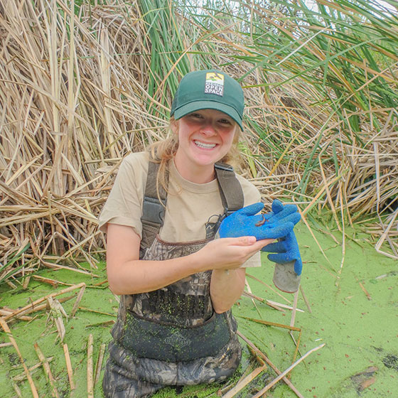 woman in pond wearing waders and holding a newt