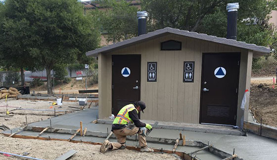 A worker smooths cement in front of a newly installed restroom