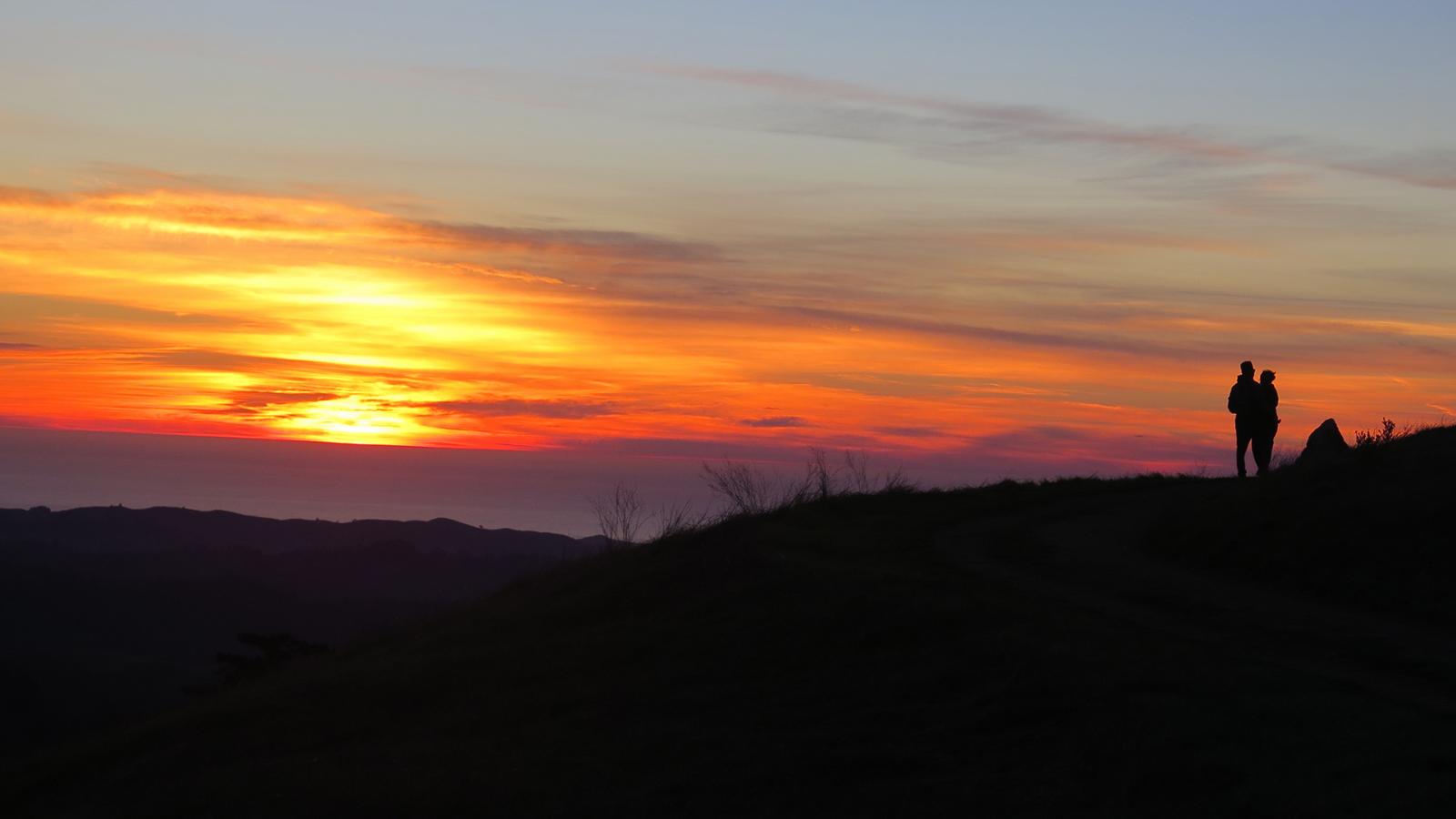 Hikers on the Windy Hill ridge at sunset, the valley glowing below