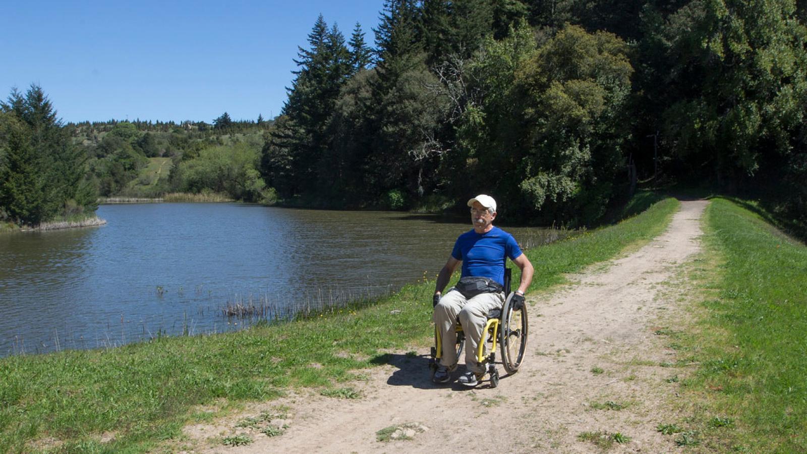 a man in a wheelchair on a trail next to a pond