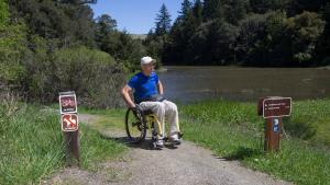 a man in a wheelchair on a trail next to a pond