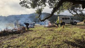 Santa Clara County Fire staff burn small piles of vegetation in a clearing by a gravel road