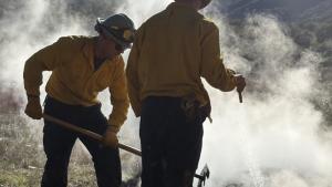 Two Santa Clara County Fire staff members use a hose and rake to stop pile burn