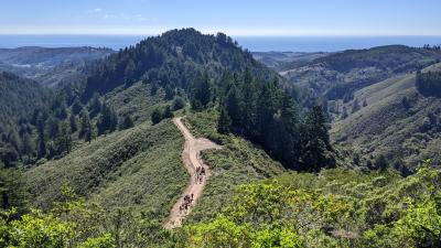 A view including a trail, forested mountains and the Pacific Ocean beyond. 