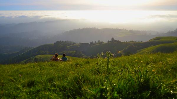 two people sitting on a grassy hill