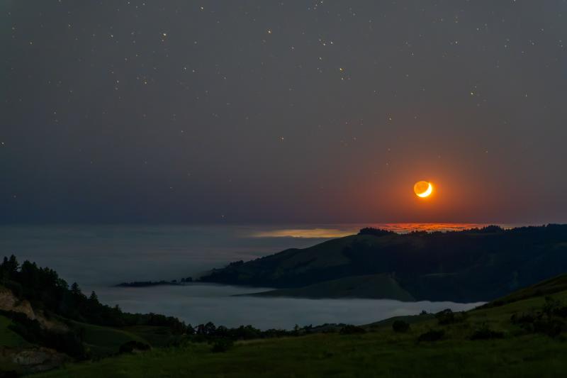 (Hsiu Ju Hsu) Orange moon in a dark sky hangs over forested mountaintops